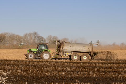 A tractor pulling a tank that spreads fertiliser over a harvested field